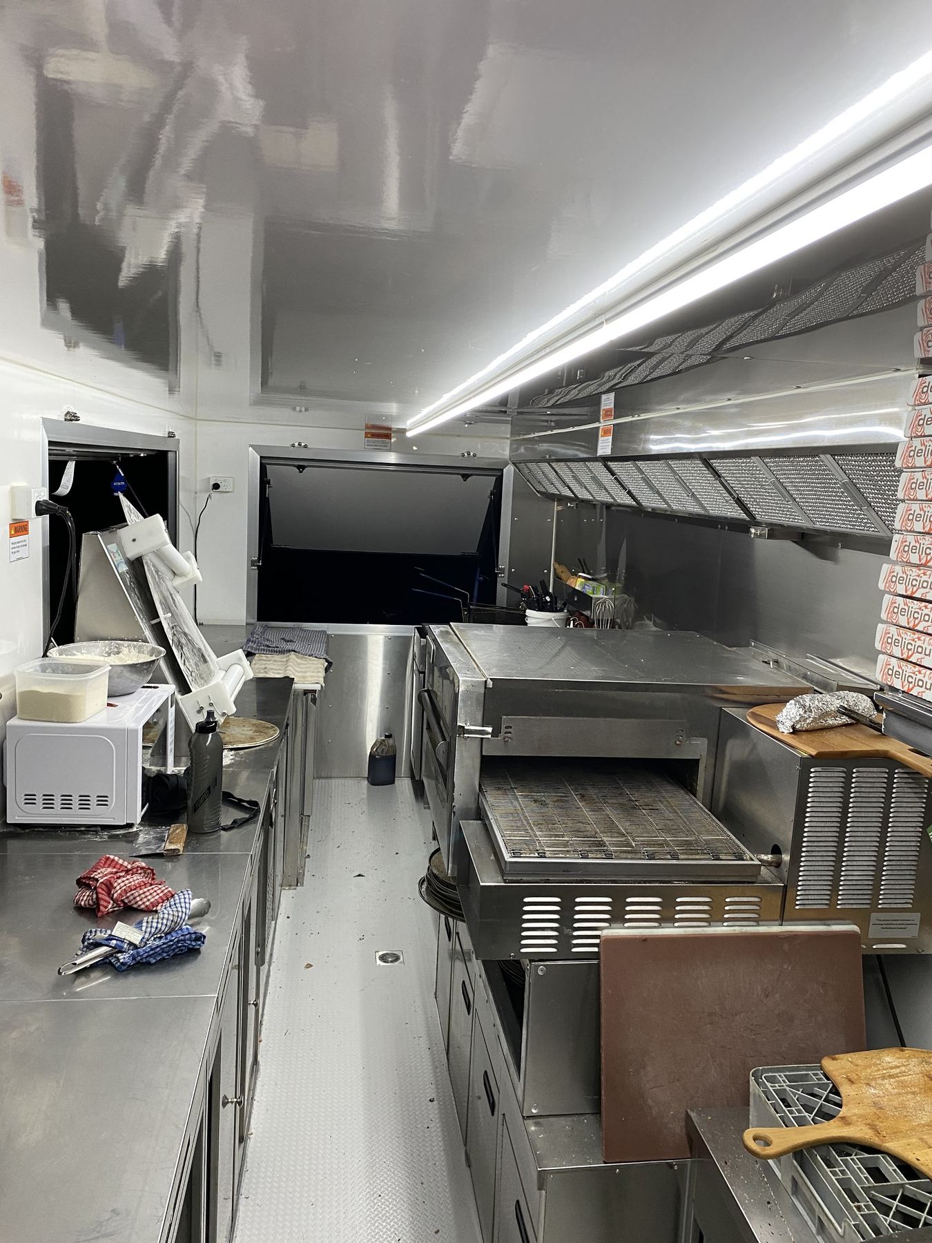 The stainless kitchen inside the Blaze Pizzas trailer with the conveyor oven and prep bench